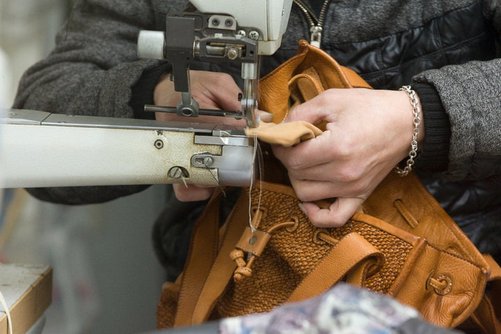 Hände nähen an einer geflochtenen Ledertasche in Cognac
