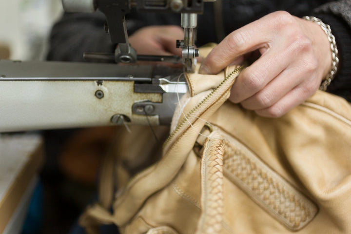 Hände führen eine helle Ledertasche mit Reißverschluss unter den Nähfuß