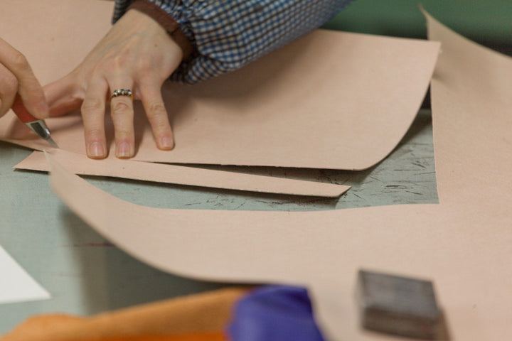 Hand schneidet ein Teil aus naturbelassenem Leder mit dem Messer zu
